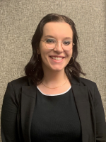 Headshot of a woman wearing glasses smiling wearing a black blazer over a black shirt.