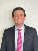 Headshot of a man smiling in a black suit, white dress shirt, and pink tie.