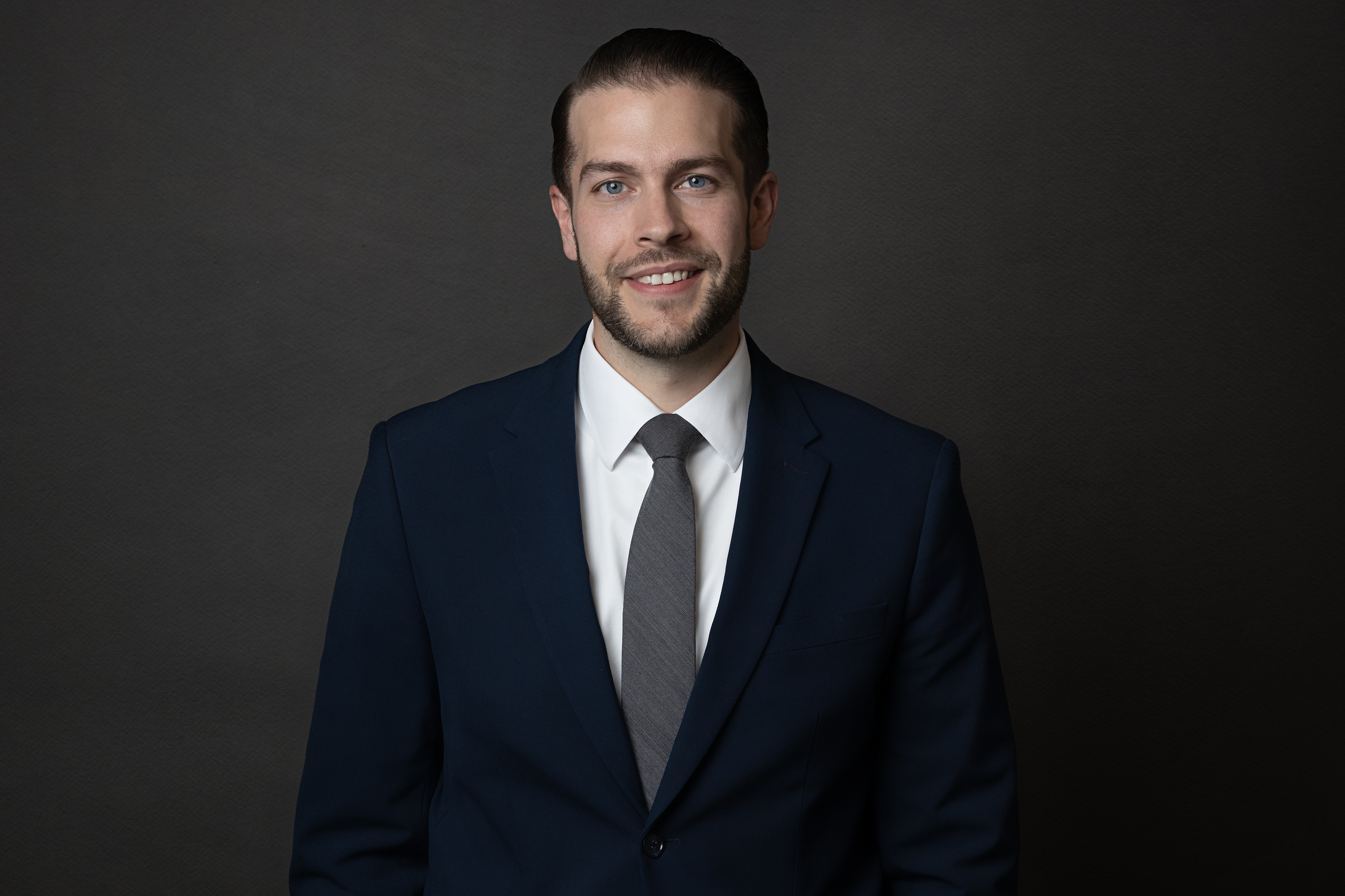 Man smiling in a navy blue suit, white collared dress s